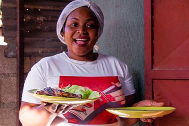 Mozambican woman holding two plates of food, smiling