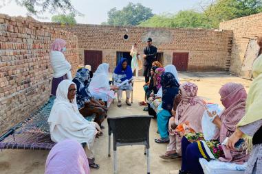 Photo of a group of women in Pakistan sitting outside in a communal space and talking. A man watches.
