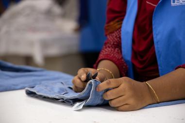 Photo showing the hands of a garment worker in Bangladesh as they work on a pair of jeans