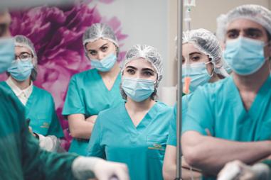 Photo of doctors in an operating theatre wearing masks. A woman in is the centre