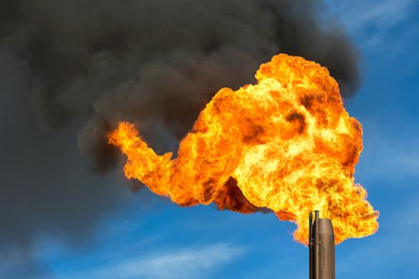 Close up photo of a gas flare with a large flame and billowing smoke