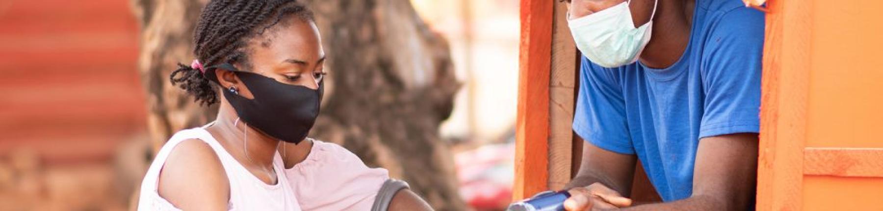 Photo a woman in Africa making a purchase via a handheld device wearing a mask