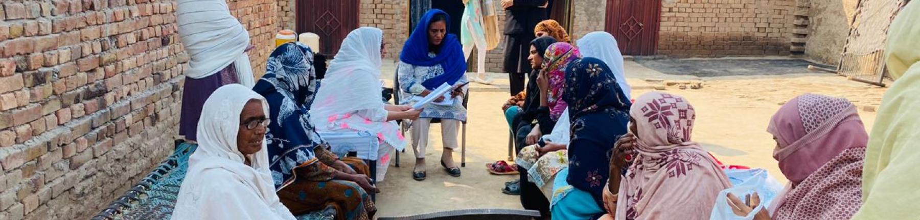 Photo of a group of women in Pakistan sitting outside in a communal space and talking. A man watches. 