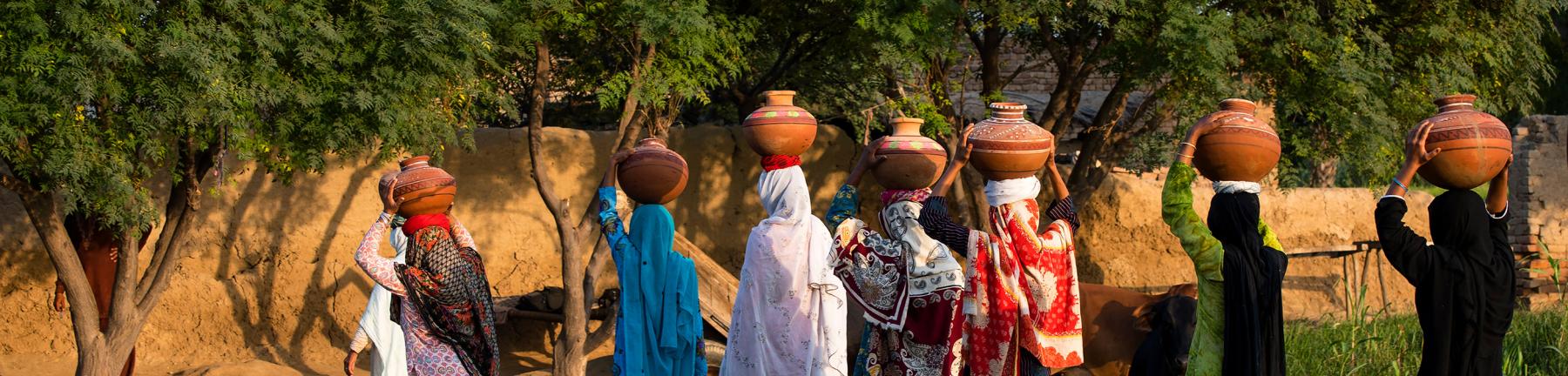 Women walking through rural Pakistan carrying jugs of water on their heads