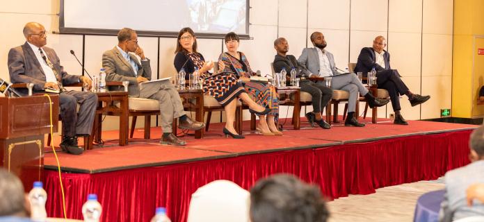 six speakers on a podium speaking on a panel